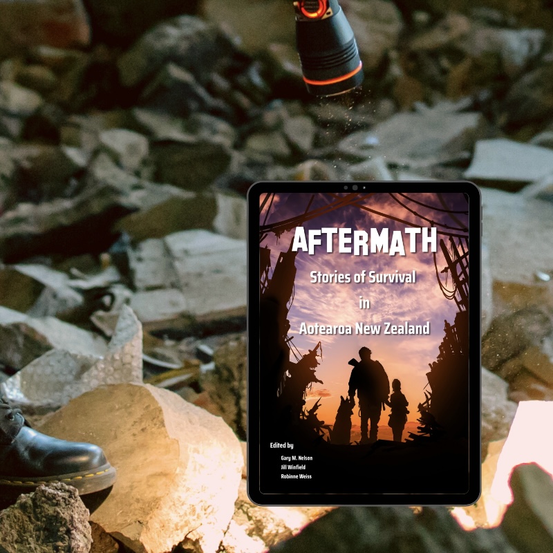 A flashlight shines down on a tablet with the eBook version of "Aftermath: Stories of Survival in Aotearoa New Zealand" amongst the rubble of a collapsed building